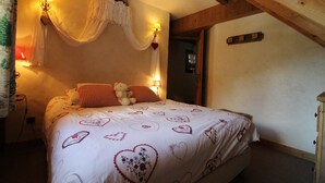 A cozy bedroom with a bed, two bedside lamps, a decorative wall hanging, and a wooden ceiling beam. - Les Cimes - Five Bedroom Apartment, Sleeps 10 (Vaujany)