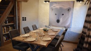 A dining area with a long table set for six, surrounded by chairs. A bookshelf is visible to the left, and a large polar bear painting is on the wall behind the table. - Les Cimes - Five Bedroom Apartment, Sleeps 10 (Vaujany)