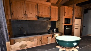 A kitchen with wooden cabinets, a black countertop, a sink, a stove, and a white refrigerator. - Les Cimes - Five Bedroom Apartment, Sleeps 10 (Vaujany)