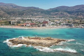 A coastal town with a beach, buildings, and mountains in the background. - Golden Bay Apartments-garden Haven (Hersonissos)