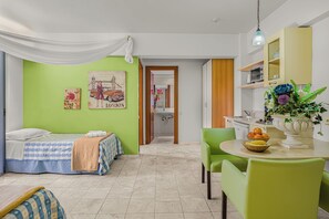 A room with a bed, a dining table with chairs, a sink, and a mirror. - Golden Bay Apartments-garden Haven (Hersonissos)