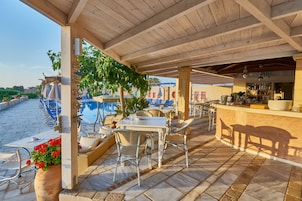 Un patio al aire libre con mesas y sillas, una zona de bar y una piscina al fondo.