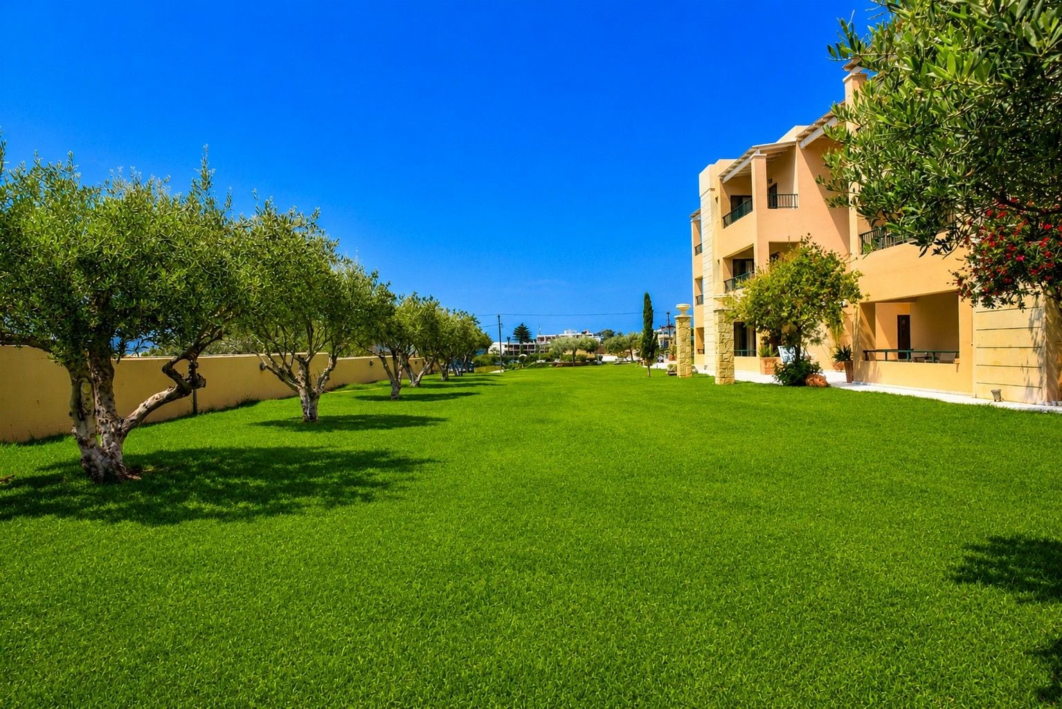 A courtyard with a well-maintained lawn, a building with balconies, and a clear blue sky.