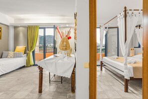 A hotel room with a bed, a table, and a view of the outdoors. - Golden Bay Apartments-garden Haven (Hersonissos)
