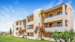 A multi-story hotel with balconies, a well-maintained lawn, and a clear sky. - Golden Bay Apartments-garden Haven (Hersonissos)