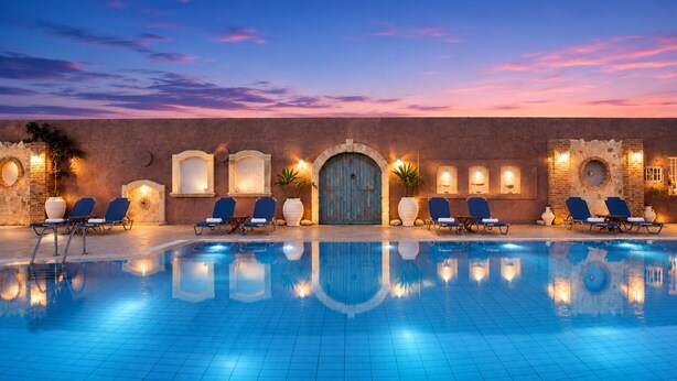 A swimming pool with lounge chairs, a stone wall, and a blue door. - Golden Bay Apartments-garden Haven (Hersonissos)