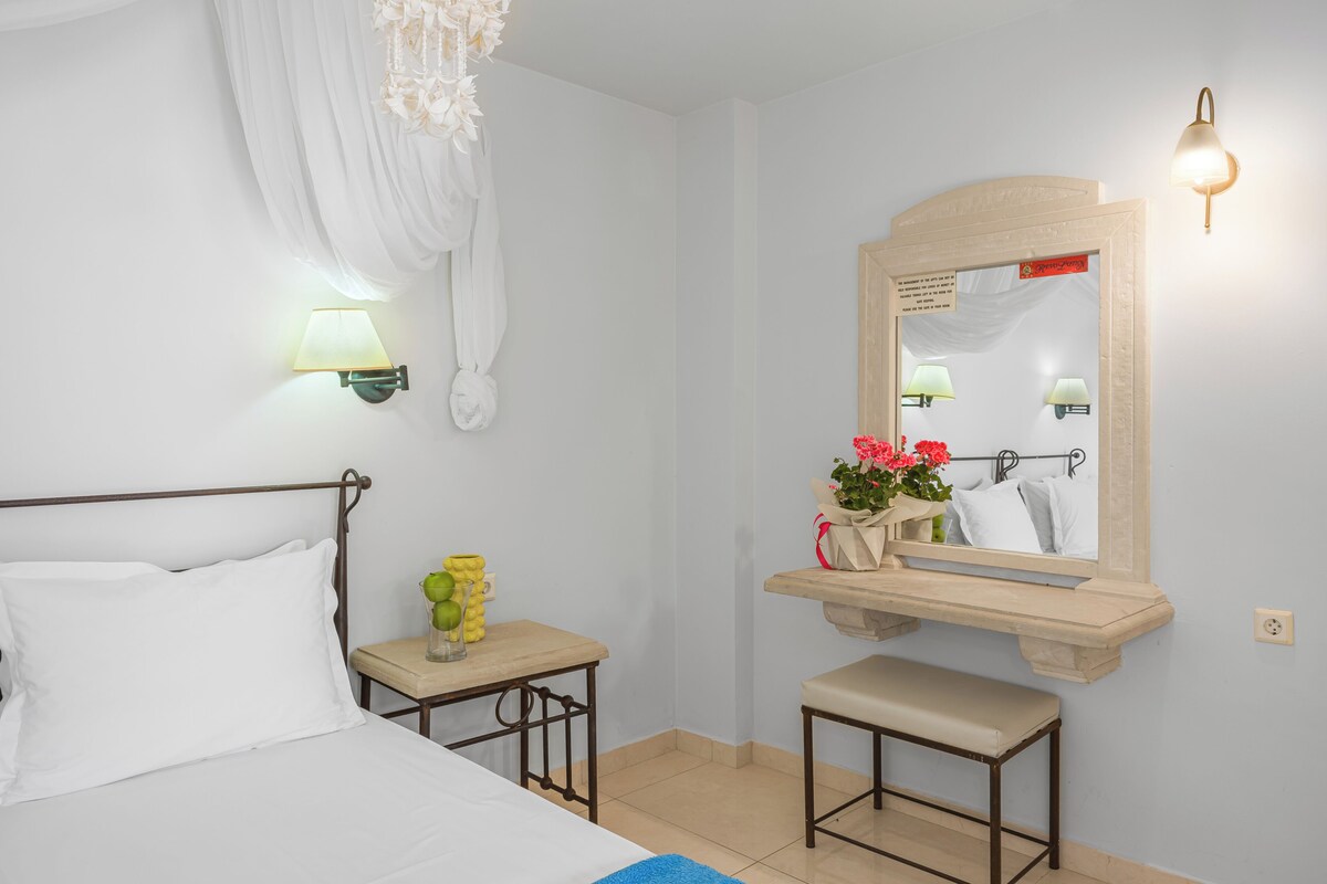 A bedroom with a bed, bedside table, bench, mirror, and wall-mounted lamps.