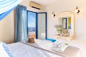 A hotel room with a bed, a mirror, a window with curtains, an air conditioning unit, and a view of the outside. - Golden Bay Apartments-garden Haven (Hersonissos)