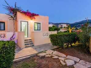 A building with a stone pathway leading to a door, surrounded by greenery and a view of distant hills. - Golden Bay Apartments-garden Haven (Hersonissos)