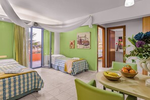 A hotel room with two beds, a dining table with fruit, and a view of the outside. - Golden Bay Apartments-garden Haven (Hersonissos)