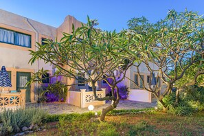 A courtyard with a tree, a pool, and a building with a balcony. - Golden Bay Apartments-garden Haven (Hersonissos)