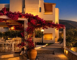 A modern building with a covered outdoor seating area, steps leading to the entrance, and a view of the surrounding landscape. - Golden Bay Apartments-garden Haven (Hersonissos)