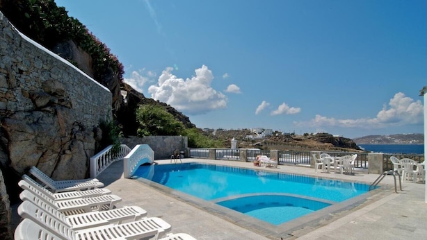 Una piscina con sillas de descanso, un muro de piedra y vista al mar.