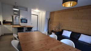 A modern kitchen with a wooden dining table, white chairs, and a built-in oven.