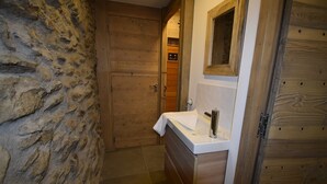 Un baño con pared de piedra, puerta de madera y un lavabo blanco con un espejo encima.