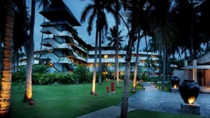 A multi-story hotel with a modern design, featuring a central courtyard surrounded by palm trees and well-lit pathways. - Santosa Villas & Resort (Senggigi)