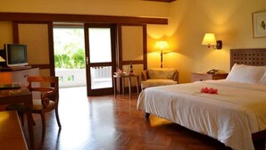A hotel room with a bed, a desk with a television, a chair, a nightstand, and a lamp. - Santosa Villas & Resort (Senggigi)