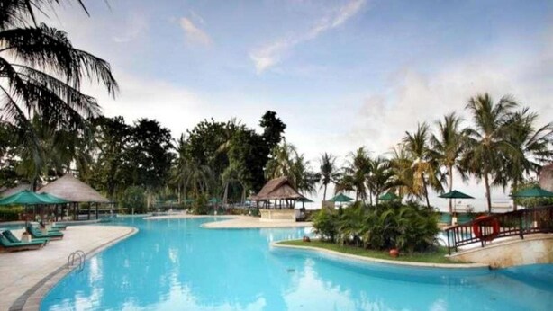 A large, clear swimming pool surrounded by palm trees and lounge chairs. - Santosa Villas & Resort (Senggigi)