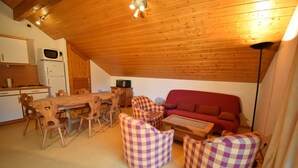 A cozy, wooden-floored living room with a dining table, chairs, a sofa, and a small table.