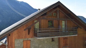 A wooden chalet with a stone foundation, a balcony, and a mountain backdrop.