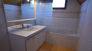 A bathroom with a white sink, mirror, and vanity. There is a window with blinds, a bathtub, and a toilet.