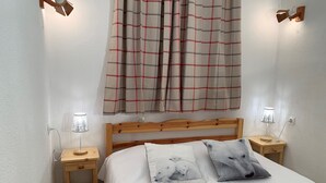 Ein Schlafzimmer mit hölzernem Kopfteil, einem Bett mit weißer Bettwäsche, zwei Nachttischen mit Lampen, einem Karomuster-Vorhang und Wandleuchten.