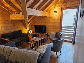Interior acogedor de una cabaña con techo de madera, un sofá, una silla, una mesita de centro y un televisor.