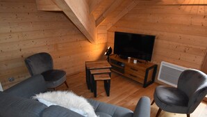 Ein gemütliches Blockhaushaus-Interieur mit Holzboden, einem Fernseher auf einem Holztisch und zwei grauen Sesseln.