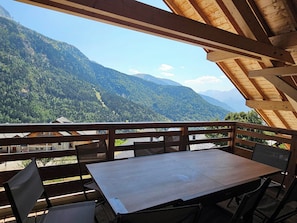 Une terrasse en bois avec une table et des chaises, d’où l’on peut admirer un paysage montagneux.
