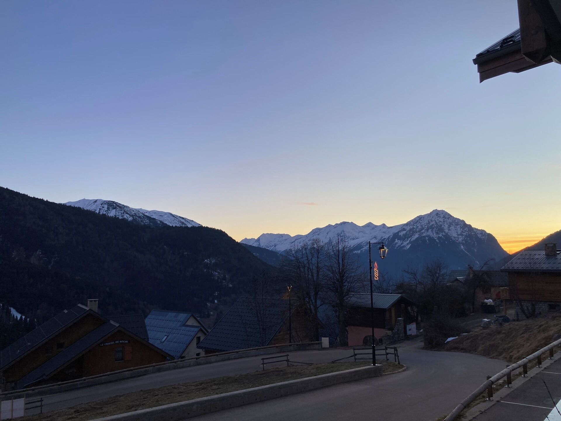 Un village de montagne aux sommets enneigés, aux bâtiments en bois et sous un ciel dégagé.