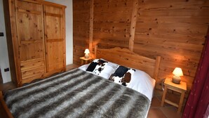 A wooden cabin room with a bed, two nightstands with lamps, a wooden wardrobe, and a red curtain.