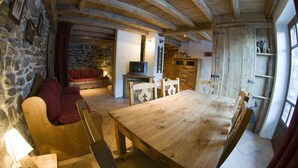 A rustic interior with a wooden dining table, stone walls, and a stone fireplace.