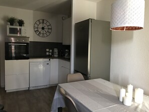 Uma cozinha moderna com micro-ondas, forno, máquina de lavar loiça e frigorífico. Há um relógio na parede e uma mesa de jantar com velas.