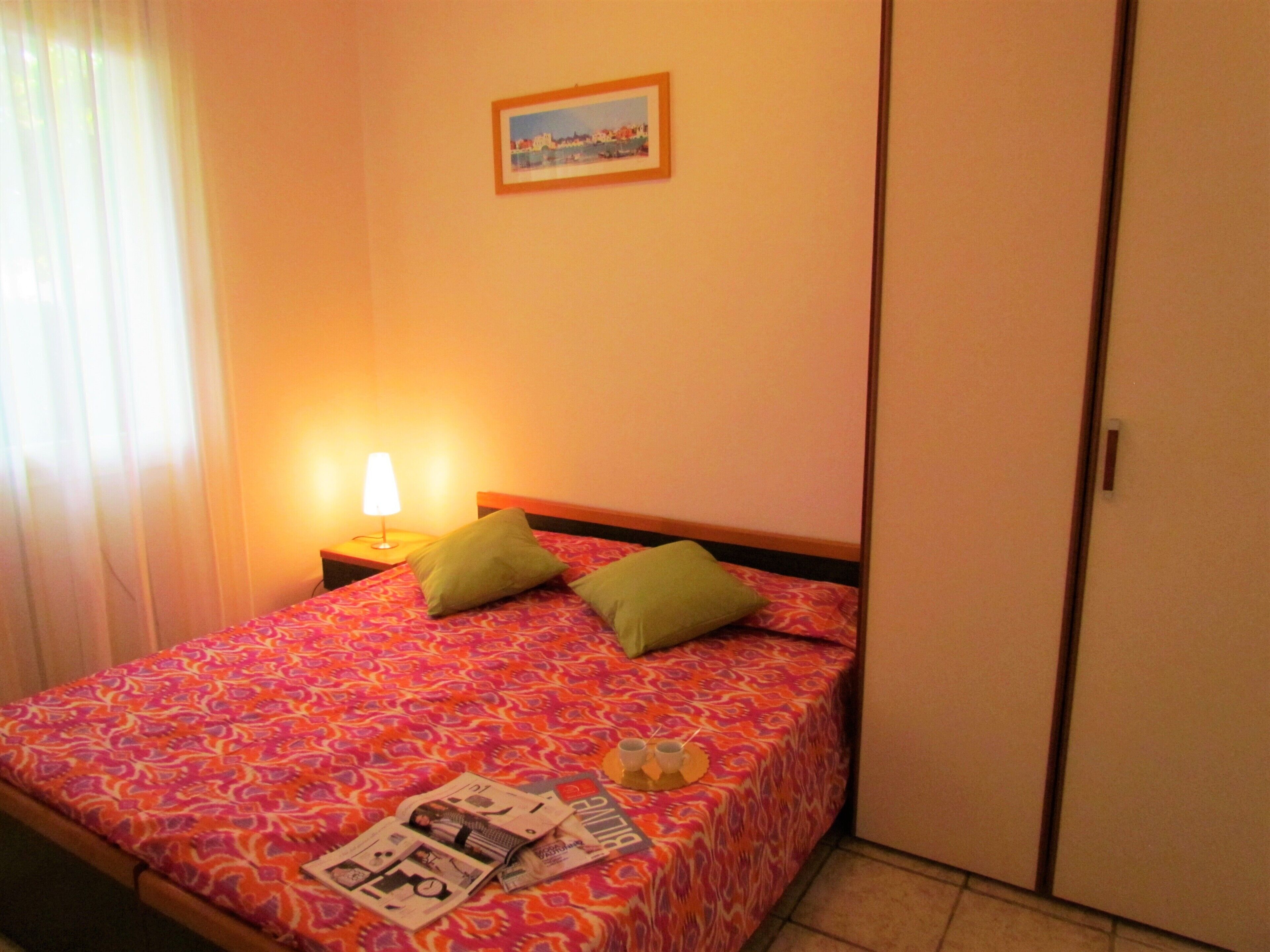 A neatly made bed with a patterned bedspread, two pillows, and a bedside lamp.
