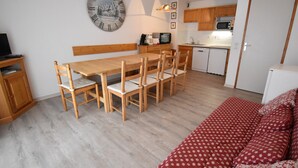 Un espace de vie compact comprenant un coin repas, une kitchenette et un canapé rouge à motifs.
