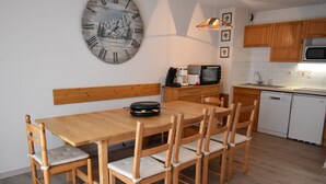 Une cuisine de taille modeste, avec une table et des chaises en bois, une grande horloge murale et les appareils électroménagers de base.