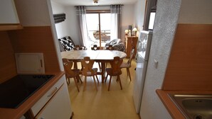 Una cocina compacta con una mesa de comedor, sillas de madera, un refrigerador y una ventana con cortinas.