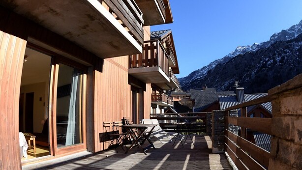 Una terraza de madera con mobiliario exterior y vistas a montañas nevadas.
