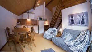Un interior acogedor con una mesa de comedor de madera, sillas, un sofá, una cocina con armarios blancos, un microondas y una escalera.