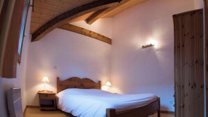 Un dormitorio con una cama de madera, dos lámparas de noche, un armario de madera y un techo inclinado.