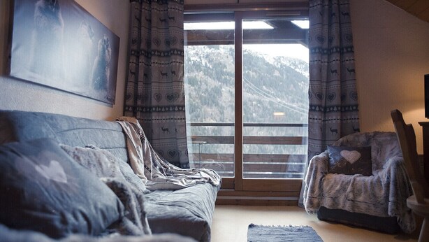 Una habitación acogedora con un ventanal grande, un sofá, una silla y un cuadro en la pared.