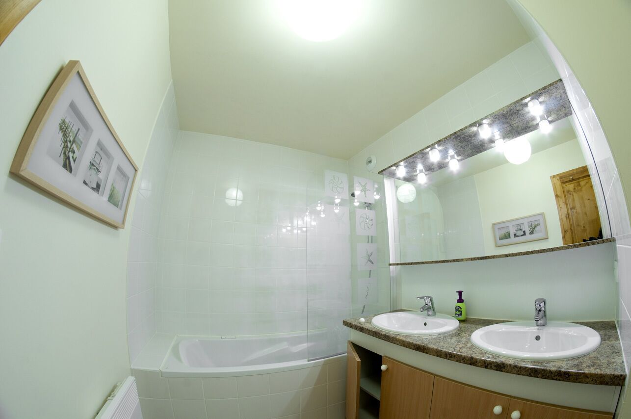 A bathroom with a bathtub, two sinks, a large mirror, and a framed picture on the wall.