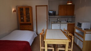 Habitació petita amb llit, taula de dinar amb cadires, cuineta equipada amb microones i torradora, i un armari de fusta.
