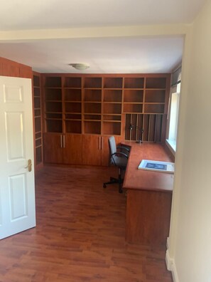 Una habitación con un escritorio de madera, una silla y un amplio estante empotrado.