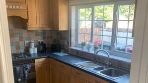 A kitchen with wooden cabinets, a double sink, and a window with a view of the outside. - 3 bedroom house in Reading (Reading)