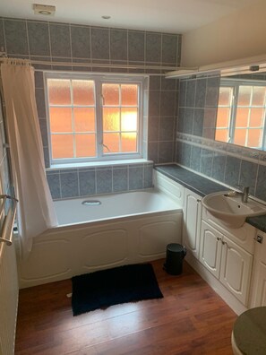 Un baño con bañera, una ventana de vidrio esmerilado, un lavamanos y un espejo.