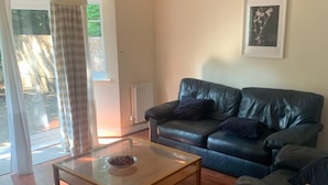 A living room with a leather sofa, a glass coffee table, and a wooden side table. - 3 bedroom house in Reading (Reading)