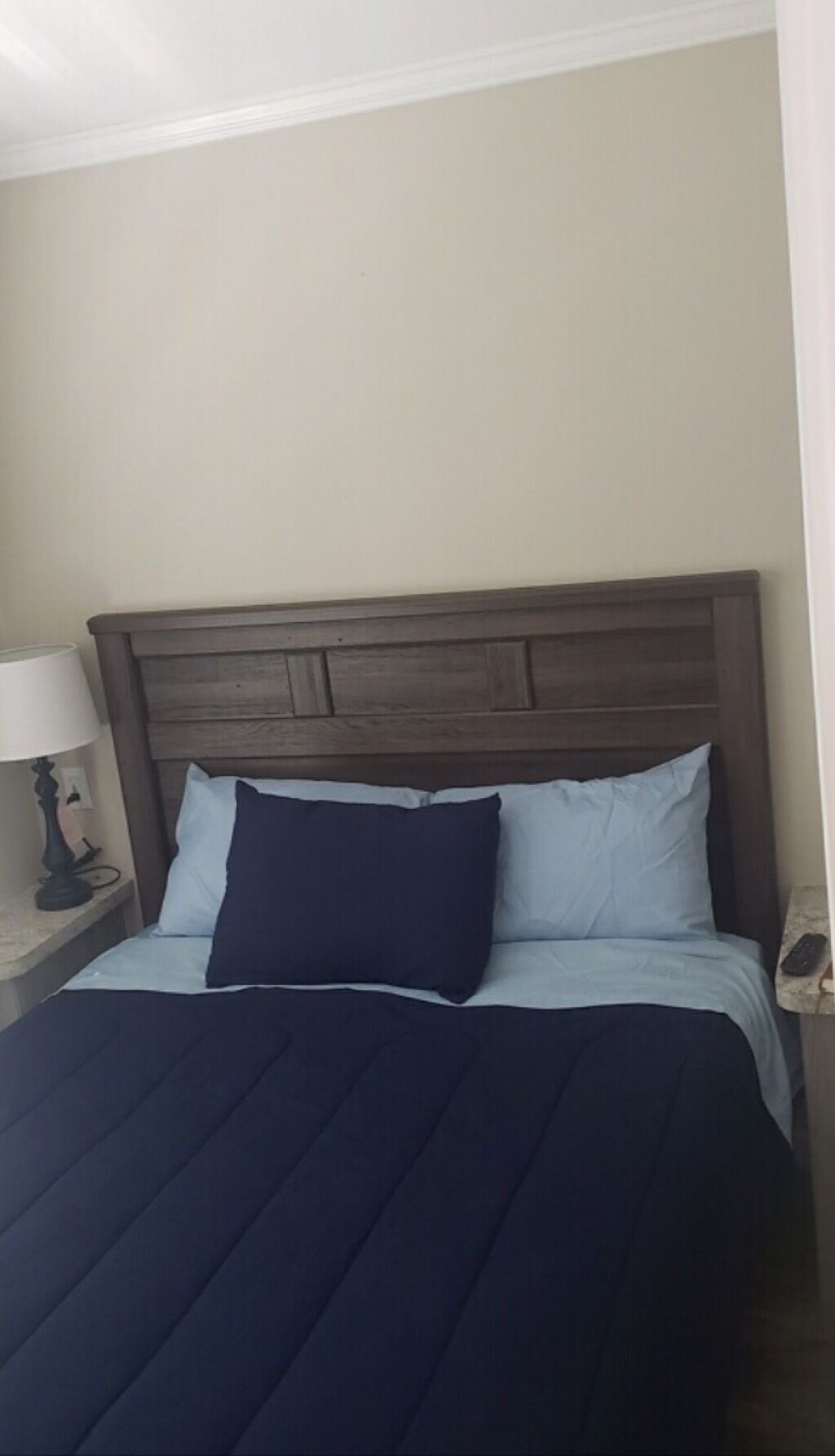 A bed with a dark headboard, light blue bedding, and a dark blue throw blanket.