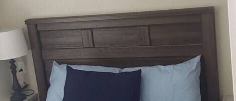 A bed with a dark headboard, light blue bedding, and a dark blue throw blanket.