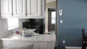 A compact kitchen with a sink, countertop, and cabinets. There is a trash can and a dining area visible. - Perfect place to call a Timeout! 3 beaches within 15 minutes! With a pool! (Venice)